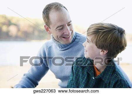 Mid adult man looking at his son and smiling View Large Photo Image Stock Image - Mid adult man looking at his son and smiling. Fotosearch