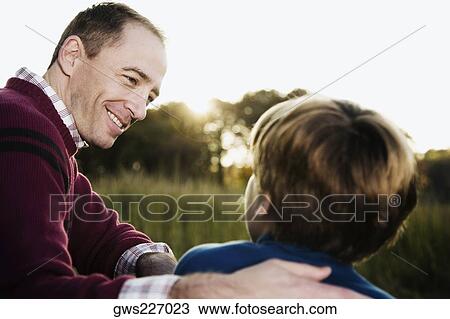 Mid adult man sitting with his son and smiling View Large Photo Image Stock Image - Mid adult man sitting with his son and smiling. Fotosearch
