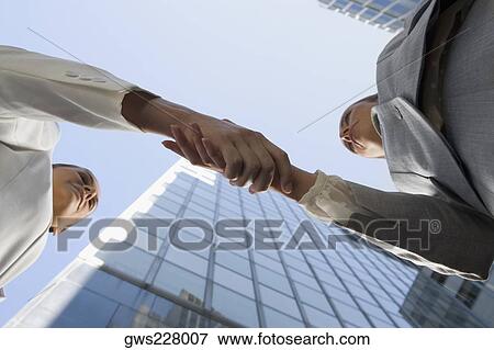 Stock Photo - Low angle view of two businesswomen shaking hands. Fotosearch