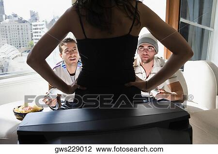 Rear view of a young woman standing in front of a television and two young men looking at her View Large Photo Image Stock Image - Rear view of a young woman standing in front of a television and two young men looking at her. Fotosearch