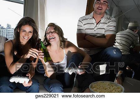 Two young women toasting with beer bottles and a young man standing beside them View Large Photo Image Stock Image - Two young women toasting with beer bottles and a young man standing beside them. Fotosearch