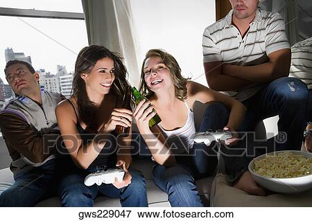 Stock Photo - Two young women toasting with beer bottles and two young men sitting beside them. Fotosearch