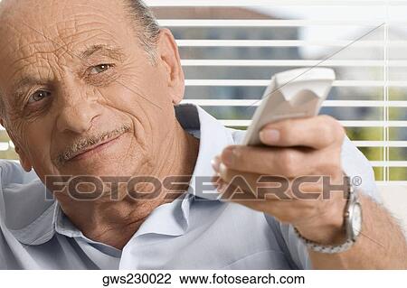 Stock Image - Close-up of a senior man operating a remote control. Fotosearch