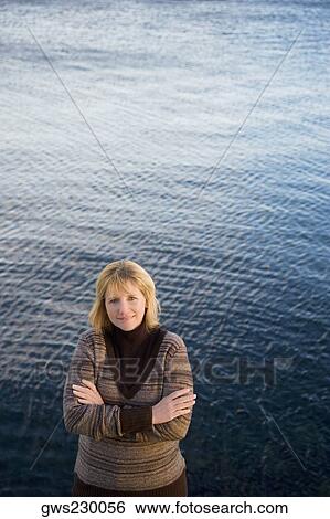 Stock Photograph - Portrait of a mature woman standing with her arms crossed and smiling. Fotosearch