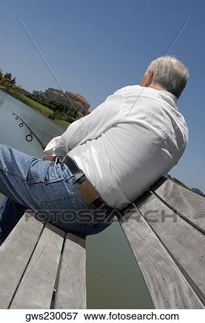 Rear view of a senior man sitting on a bench at the lakeside and fishing View Large Photo Image Stock Photo - Rear view of a senior man sitting on a bench at the lakeside and fishing. Fotosearch