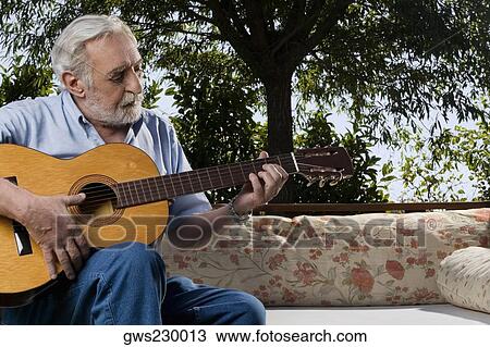 Stock Image - Senior man sitting on a couch and playing a guitar. Fotosearch