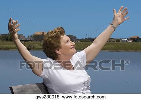 Senior woman sitting at the lakeside with arms outstretched View Large Photo Image Stock Photo - Senior woman sitting at the lakeside with arms outstretched. Fotosearch