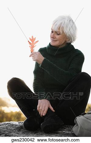 Senior woman sitting on a rock and looking at a leaf View Large Photo Image Stock Image - Senior woman sitting on a rock and looking at a leaf. Fotosearch