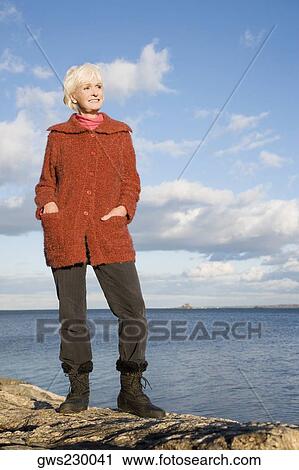 Stock Image - Senior woman standing on a rock at seaside. Fotosearch