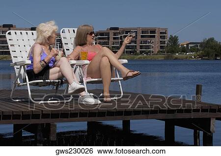 Stock Photograph - Two senior women sitting on chairs at the boardwalk. Fotosearch