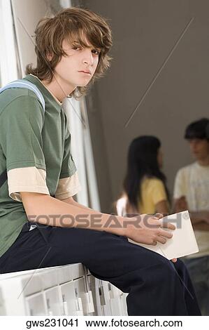 Portrait of a teenage boy sitting on a cabinet and looking serious View Large Photo Image Stock Image - Portrait of a teenage boy sitting on a cabinet and looking serious. Fotosearch