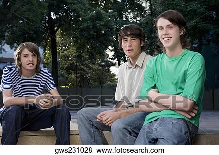 Stock Photo - Portrait of two teenage boys sitting with a young man and smiling. Fotosearch