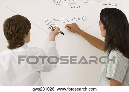 Rear view of a teenage boy solving algebra on whiteboard and a female teacher standing beside him View Large Photo Image Stock Photograph - Rear view of a teenage boy solving algebra on whiteboard and a female teacher standing beside him. Fotosearch