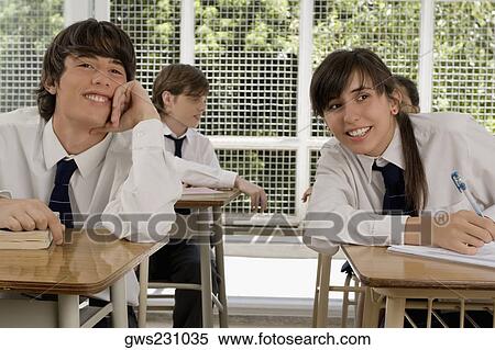 Stock Photography - Teenage girl and a young man sitting in a classroom and smiling. Fotosearch