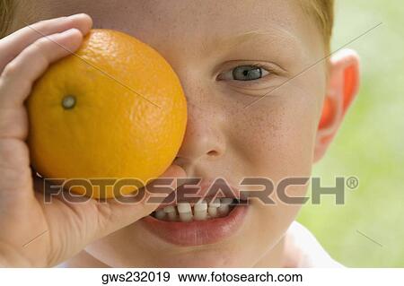 Portrait of a boy holding an orange over his eye View Large Photo Image Stock Photo - Portrait of a boy holding an orange over his eye. Fotosearch