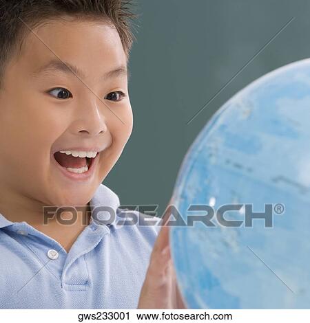 Stock Image - Close-up of a schoolboy looking at a globe and laughing. Fotosearch