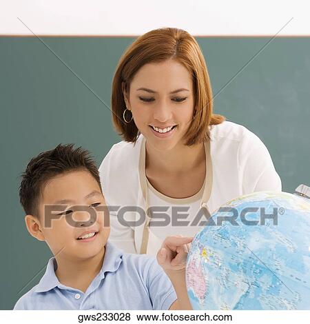 Stock Photo - Close-up of a schoolboy with his teacher looking at a globe and smiling. Fotosearch