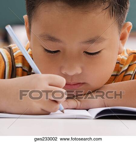 Stock Image - Close-up of a schoolboy writing on a notebook with a pencil. Fotosearch