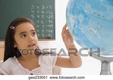 Stock Image - Close-up of a schoolgirl looking at a globe in a classroom. Fotosearch