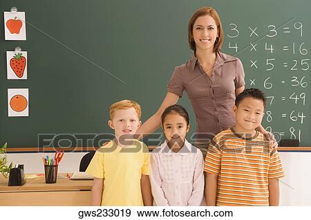 Portrait of a female teacher standing with her three students in a classroom View Large Photo Image Stock Photo - Portrait of a female teacher standing with her three students in a classroom. Fotosearch