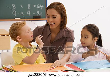 Schoolgirl and a schoolboy with their female teacher sitting in a classroom View Large Photo Image Stock Photograph - Schoolgirl and a schoolboy with their female teacher sitting in a classroom. Fotosearch