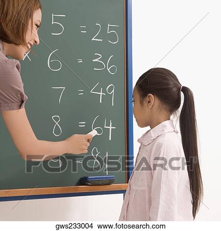 Side profile of a female teacher teaching a schoolgirl on a blackboard View Large Photo Image Picture - Side profile of a female teacher teaching a schoolgirl on a blackboard. Fotosearch