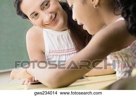 Female teacher teaching her student in a classroom View Large Photo Image Picture - Female teacher teaching her student in a classroom. Fotosearch