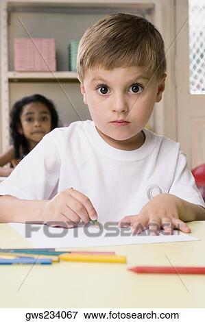 Stock Photo - Portrait of a boy drawing on a sheet of paper with a girl sitting behind him. Fotosearch