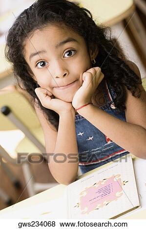 Stock Photo - Portrait of a girl sitting at a desk with her hands on her chin. Fotosearch