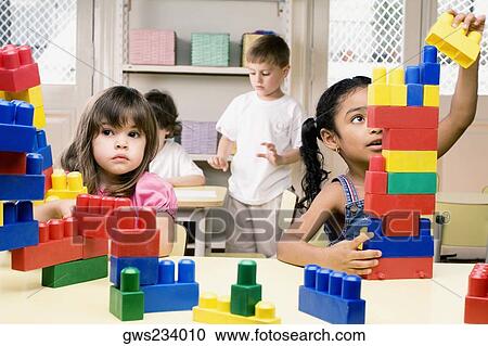 Two girls playing with plastic blocks with their friends in the background View Large Photo Image Stock Image - Two girls playing with plastic blocks with their friends in the background. Fotosearch