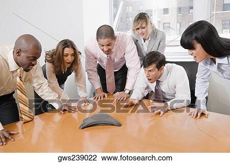 Stock Image - Business executives looking at the conference phone. Fotosearch