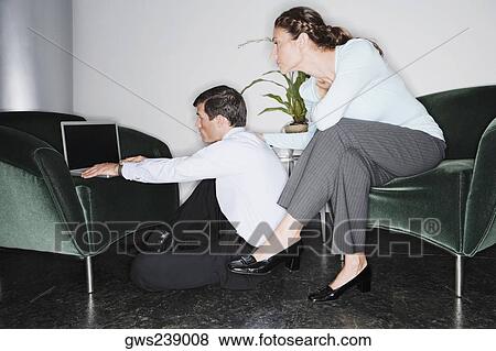 Stock Photo - Businessman using a laptop with a businesswoman sitting behind him. Fotosearch