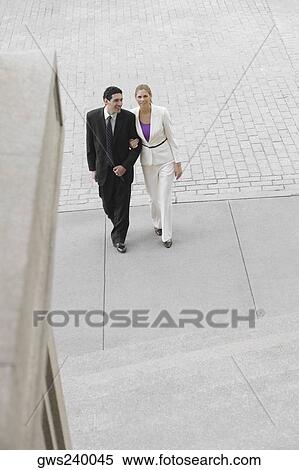 Stock Photography - Businessman and a businesswoman walking with their arm in arm. Fotosearch