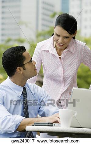 Businessman using a laptop with a businesswoman standing beside him View Large Photo Image Stock Photo - Businessman using a laptop with a businesswoman standing beside him. Fotosearch
