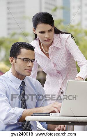 Businessman using a laptop with a businesswoman standing beside him View Large Photo Image Stock Photo - Businessman using a laptop with a businesswoman standing beside him. Fotosearch