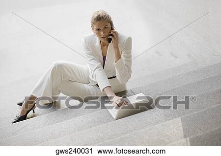 Businesswoman sitting on steps talking on a mobile phone and using a laptop View Large Photo Image Stock Image - Businesswoman sitting on steps talking on a mobile phone and using a laptop. Fotosearch