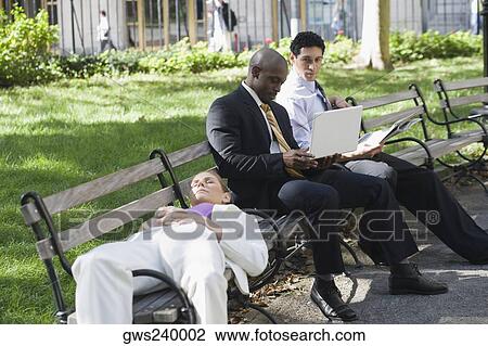 Businesswoman sleeping on a bench with two businessmen sitting beside her and looking at a laptop View Large Photo Image Stock Image - Businesswoman sleeping on a bench with two businessmen sitting beside her and looking at a laptop. Fotosearch
