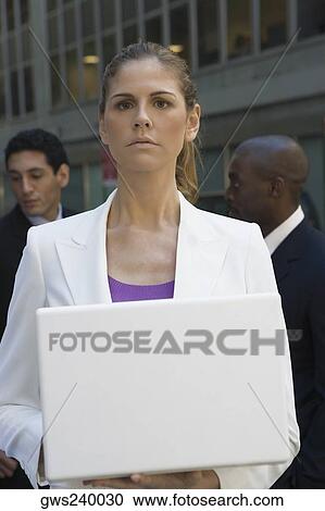 Close-up of a businesswoman holding a laptop with two businessmen standing behind her View Large Photo Image Stock Image - Close-up of a businesswoman holding a laptop with two businessmen standing behind her. Fotosearch