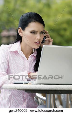 Close-up of a businesswoman talking on a mobile phone while using a laptop View Large Photo Image Stock Photo - Close-up of a businesswoman talking on a mobile phone while using a laptop. Fotosearch