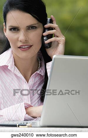 Stock Image - Portrait of a businesswoman talking on a mobile phone while using a laptop. Fotosearch
