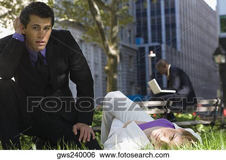 Portrait of a young woman lying on grass in a park with a businessman beside her View Large Photo Image Stock Photograph - Portrait of a young woman lying on grass in a park with a businessman beside her. Fotosearch