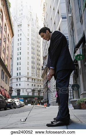 Stock Image - Side profile of a businessman playing golf on the road. Fotosearch