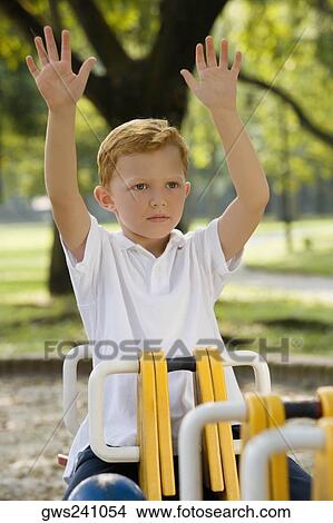 Boy sitting on a ride with his arms raised in a park View Large Photo Image Picture - Boy sitting on a ride with his arms raised in a park. Fotosearch