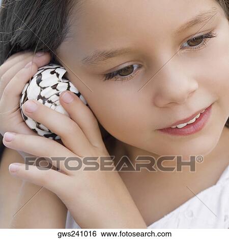 Stock Photograph - Close-up of a girl listening to shell. Fotosearch