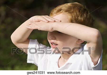 Stock Image - Close-up of a schoolboy shielding his eyes. Fotosearch