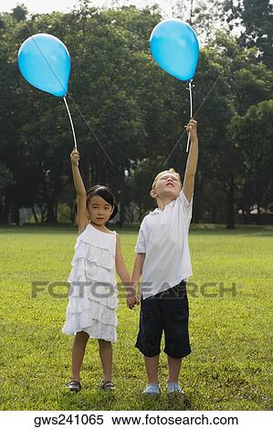 Girl with a boy standing in a park and holding balloons View Large Photo Image Stock Photography - Girl with a boy standing in a park and holding balloons. Fotosearch