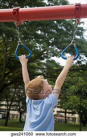 Stock Image - Rear view of a boy hanging on monkey bars. Fotosearch