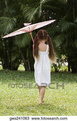 Stock Image - Rear view of a girl walking in a park with an umbrella. Fotosearch