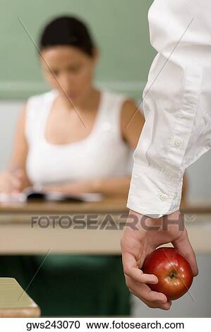 Close-up of a person's hand holding an apple with a female teacher sitting in the background View Large Photo Image Stock Image - Close-up of a person's hand holding an apple with a female teacher sitting in the background. Fotosearch