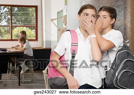Stock Photo - Close-up of a schoolgirl whispering to another schoolgirl. Fotosearch